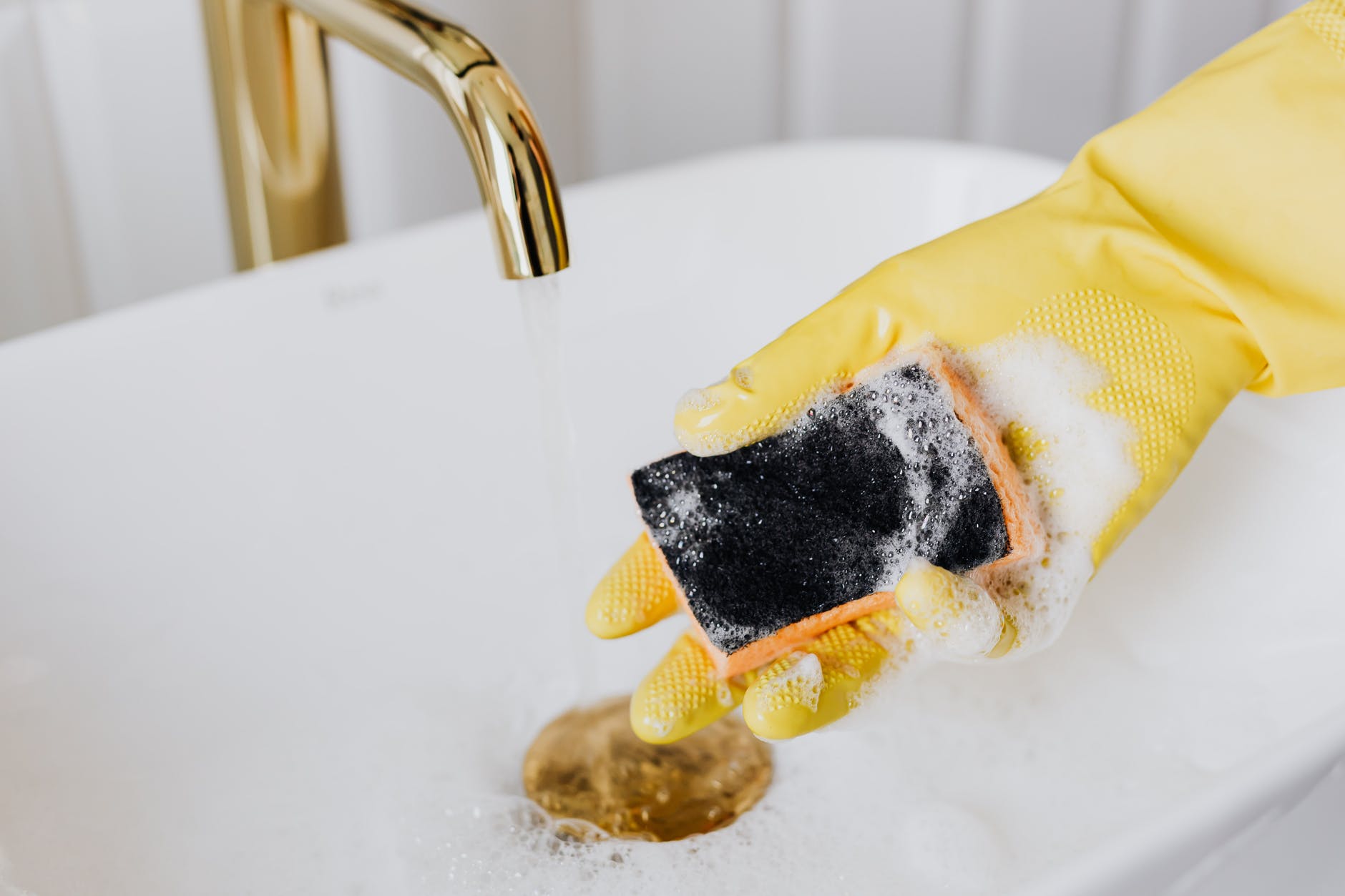 person in glove using detergent and sponge while cleaning sink