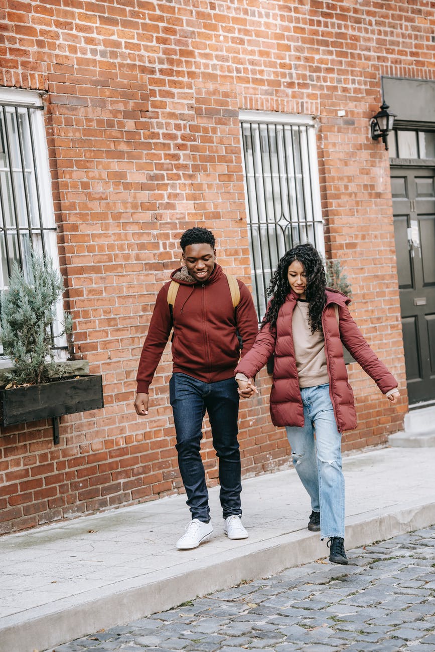 young diverse delighted couple holding hands and walking on street