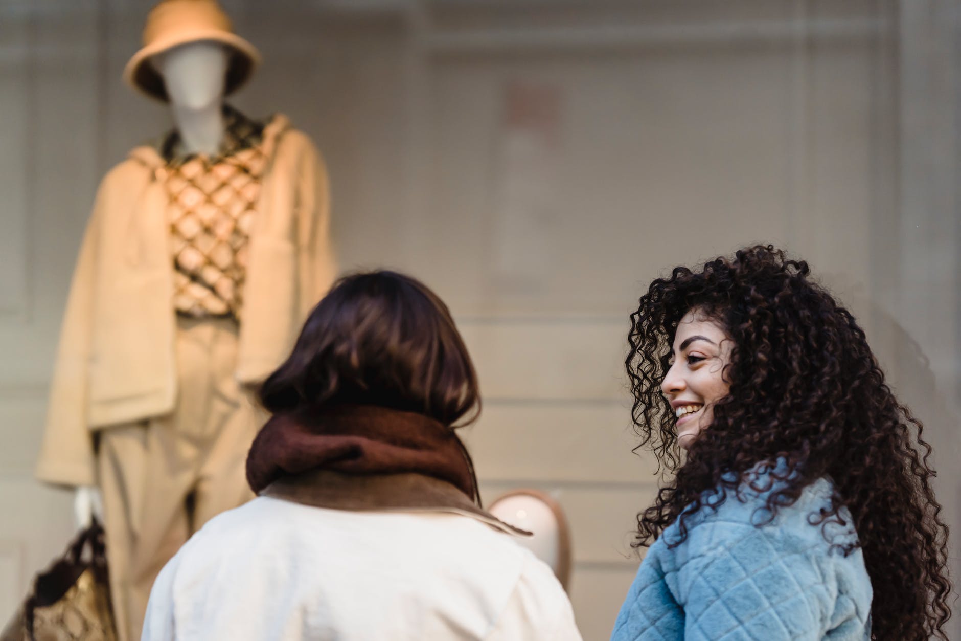 content young ethnic women smiling at street while looking at trendy clothes on mannequin