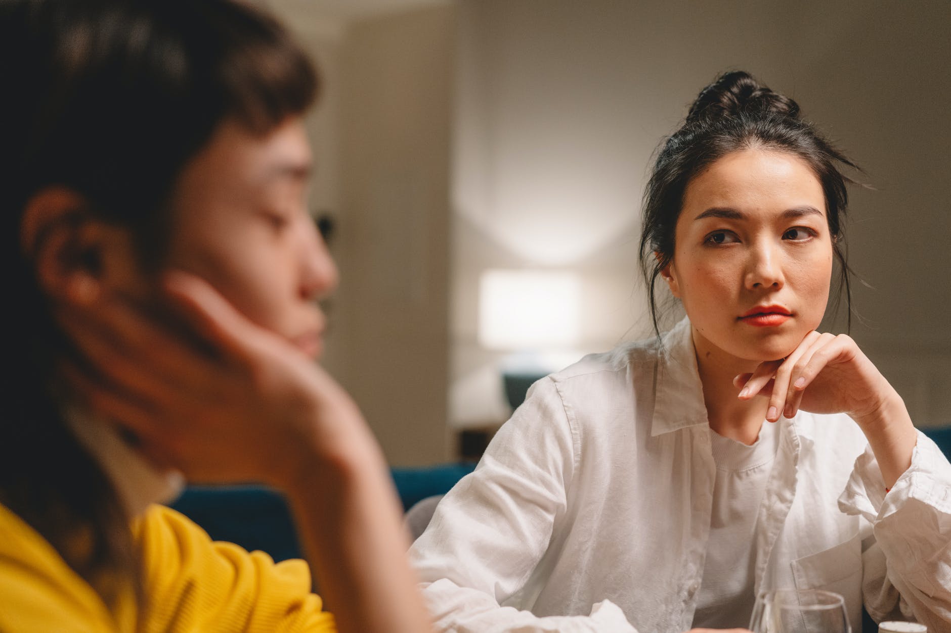 thoughtful young ethnic women having conversation at table at home