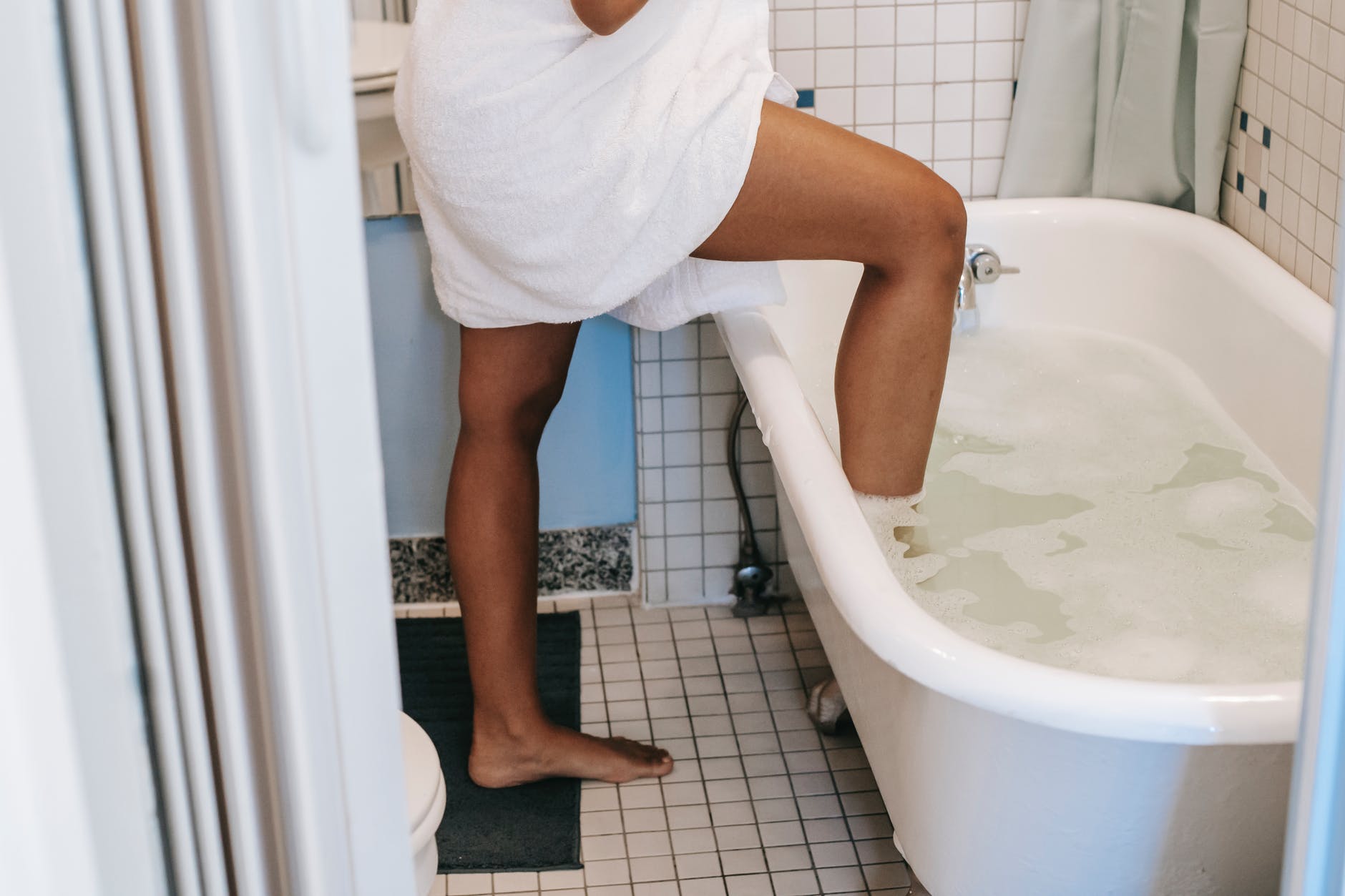 ethnic woman putting leg in bath in morning