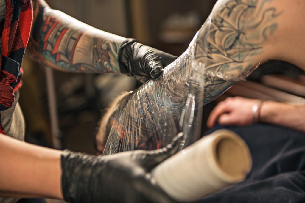 tattoo artist wrapping client s arm in plastic clingfilm to encourage tattoo healing