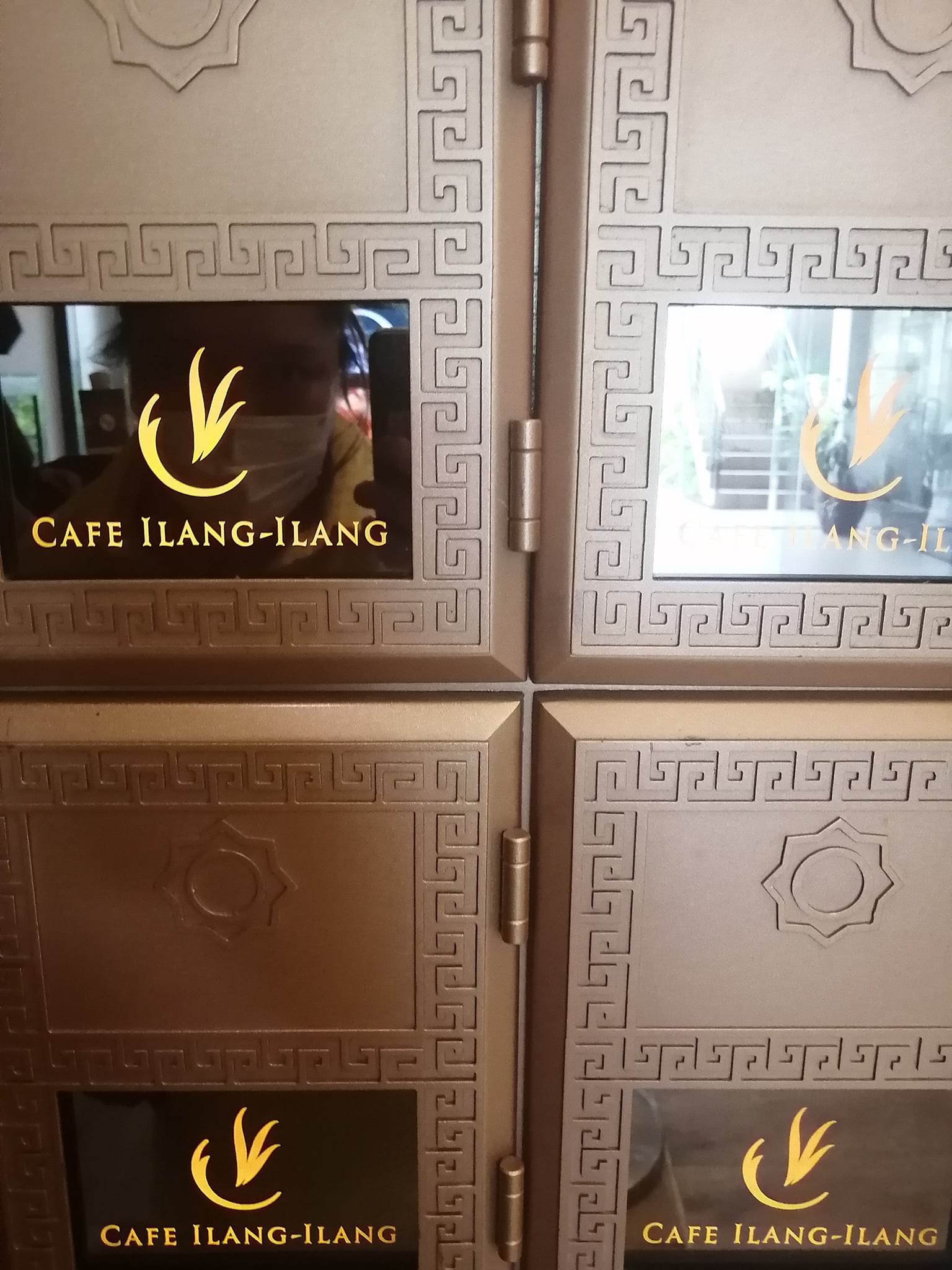 The Cafe Ilang-Ilang logo on wall details with the author reflected in one pane
